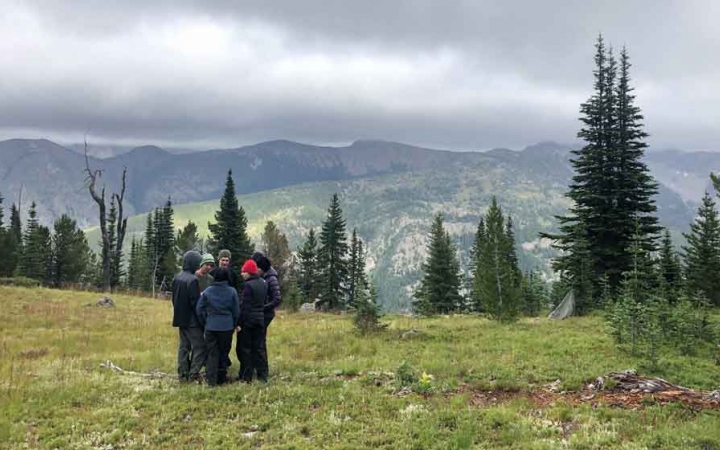 a group of students stand in a mountain meadow with a mountainous landscape in the background